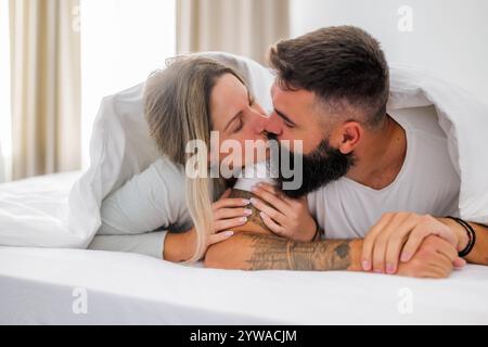 Das junge, glückliche Liebespaar liegt morgens im Bett. Sie haben Spaß und küssen sich. Stockfoto