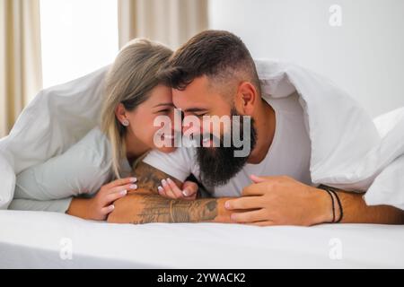 Das junge, glückliche Liebespaar liegt morgens im Bett. Sie haben Spaß und lächeln. Stockfoto