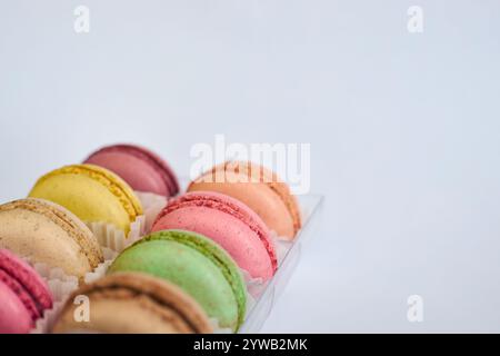 Zarte bunte Kuchen, französische Macarons mit weißer Paperpan in transparenter Plastikverpackung auf grauem Hintergrund. Appetitliches Dessert, verschiedene Maca Stockfoto