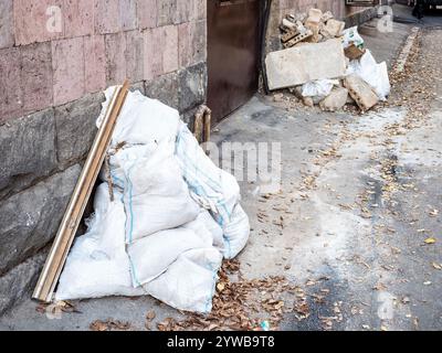 Säcke mit Bauabfällen in der Nähe des Eingangs zum Wohngebäude auf der Straße in Jerewan am Herbstabend Stockfoto