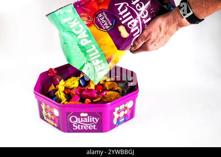 Eine Frau, die eine Tasse Quality Street Pralinen aus einer Großpackung nachfüllt. Stockfoto