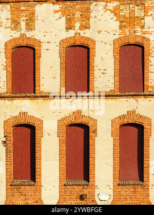 Ein Fragment der Fassade eines verlassenen historischen Backsteinhauses mit Fenstern, die mit braunen Spanplatten bedeckt sind, Konservierungsmaßnahmen Stockfoto