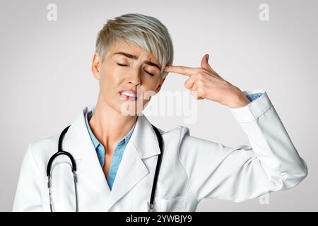 Arzt mit geschlossenen Augen schießt mit den Fingern in den Tempel Stockfoto