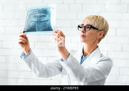 Arzt beobachtet Röntgenaufnahmen. Zahnärztin schaut auf Schnappschüsse von Zähnen auf weißem Backstein Wand Hintergrund Stockfoto