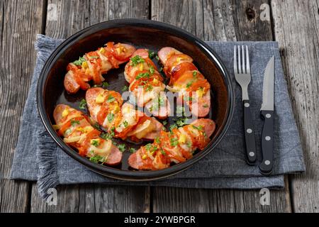 Uunimakkara, gebacken im Ofen Würstchen mit Käse, Tomaten und Senf in Backform auf grauem Holztisch mit Besteck, finnisches Retro-Rezept Stockfoto