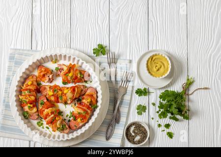 Uunimakkara, gebacken im Ofen Würstchen mit Käse, Tomaten, Koriander, Senf in Backform auf weißem Holztisch mit Zutaten, finnischer Retro Stockfoto