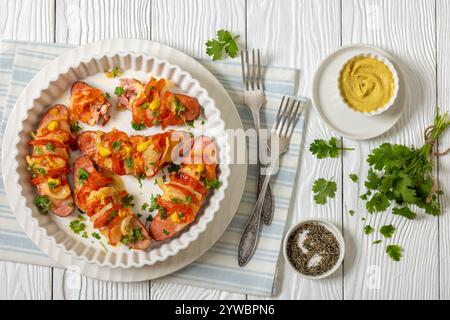 Uunimakkara, gebacken im Ofen Würstchen mit Käse, Tomaten, Koriander, Senf in Auflaufform auf weißem Holztisch mit Zutaten, finnischer Rückgabe Stockfoto