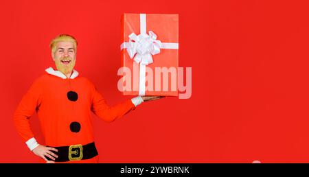 Weihnachten oder Neujahr einkaufen. Lächelnder bärtiger Mann im Weihnachtsmannkostüm mit Weihnachtsgeschenkbox. Hübscher Mann mit großem Weihnachtsgeschenk. Geschenkartikel Stockfoto