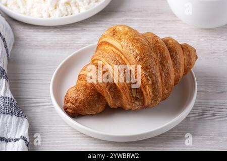 Köstliches Frühstück mit Croissant, Hüttenkäse und Kaffee auf einem Holztisch Stockfoto