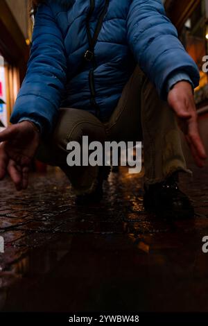 Weibliche Füße in blauen Sneakers spiegeln sich abends in einer Pfütze einer Stadtstraße Stockfoto