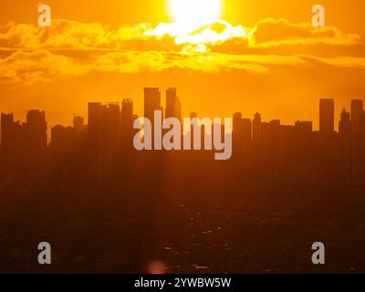 Die Skyline der Stadt Manila leuchtet im warmen Sonnenlicht der goldenen Stunde und bildet während des Sonnenuntergangs eine fesselnde Silhouette vor dem Hintergrund leuchtender orangener Wolken Stockfoto