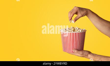 Nahaufnahme der männlichen Hände halten Einweg Eimer mit Popcorn auf orangefarbenem Hintergrund, Kopie Raum. Panorama Stockfoto