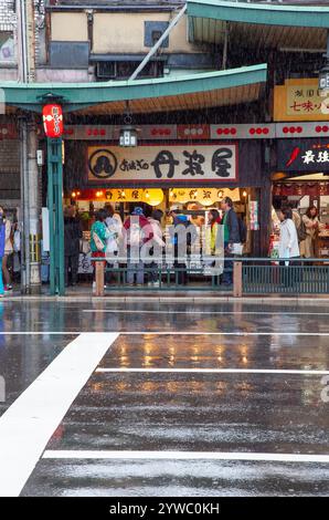 Szene mit Menschen und Verkehr auf der Shijo Street in der Innenstadt von Gion, Kyoto, Japan bei Regen. Stockfoto