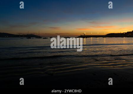 Friedlicher Sonnenuntergang am Strand von Panxón mit Booten, die in ruhigem Wasser ankern. Das sanfte Licht reflektiert das Meer und schafft eine ruhige Szene. Nigran - Galicien - Stockfoto