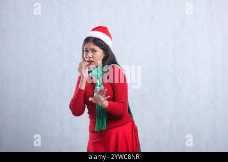 Geste einer asiatischen Teenager-Frau, die Weihnachtspullover, Weihnachtsmütze und Schal trägt, Angst vor der Kamera, Finger beißen und Schild ablehnen, isoliert auf weißem bac Stockfoto