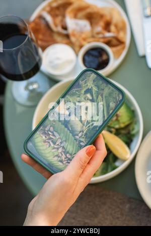 Blick von oben auf eine Frau, die ein Foto von ihrem Avocado-Salat-Mittagessen auf ihrem Handy macht Stockfoto