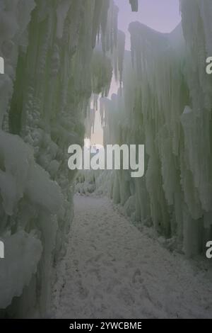 Ein schneebedeckter Pfad zwischen zwei Mauern aus gefrorenem Eis und Eiszapfen, der sich in den Ice Castles am Genfer See, Wisconsin, USA, erhebt Stockfoto