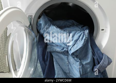 Waschmaschine mit schmutzigen Jeans und anderen Denim-Kleidern im Innenbereich Stockfoto