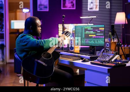 Kreativer Songwriter, der eine Melodie singt und Gitarre spielt, Signalverarbeitungstechnologie mit digitaler Audiosoftware. Künstlerproduzent, der Musik mit Akustikinstrument und Konsole kreiert. Stockfoto