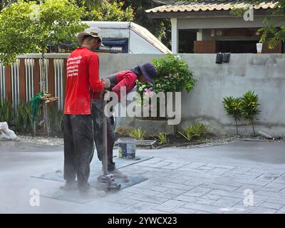 Pattaya, Thailand, 29. November 2024, qualifizierte Arbeiter tragen akribisch Stempelbeton auf, um eine strukturierte Oberfläche zu schaffen. Die lebendigen Blumen und das Grün verleihen der Szene Charme. Stockfoto