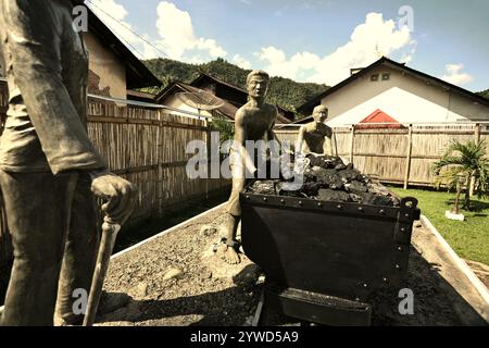 Skulpturen, die einen Aufseher zeigen, der Arbeiter beim Transport von Kohle mit einem Eisenbahnwagen in Sawahlunto, einer ehemaligen Kohlebergbaustadt in Sumatra, aufmerksam macht. Stockfoto