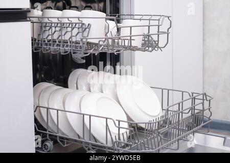 Eingebaute Geschirrspüler-Tür offen. Küche mit Einbaugeräten. Teller und Geschirr sind spülmaschinenfest. Stockfoto