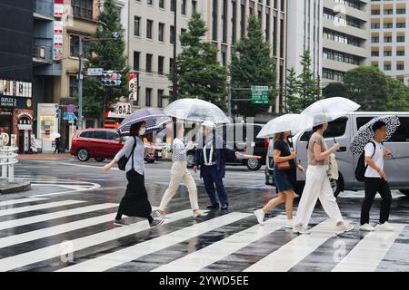 TOKIO, JAPAN - 27. September 2024: Fußgänger mit Regenschirmen, die an einem regnerischen Tag den Verkehr in Tokios Ginza-Gebiet kontrollieren. Stockfoto