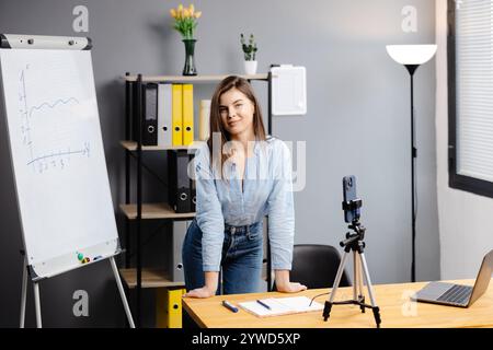 Junge Frau Mentorin nimmt Präsentationen auf, Webinar über Smartphone auf Stativ stehend, Lehrer Coach erklärt, hält Online-Unterricht, mit Telefon-Webc Stockfoto