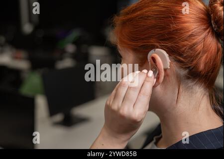 Kaukasische Frau, die im Büro ein Hörgerät auflegt. Stockfoto