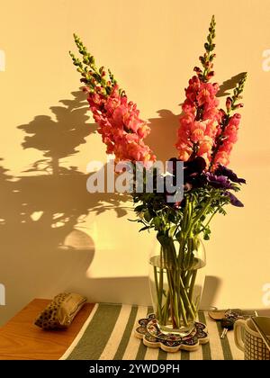 Snapdragon Blumen in Vase auf Tisch mit Schlüsseln, Bechertasche und abgestreiftem Tischtuch Stockfoto