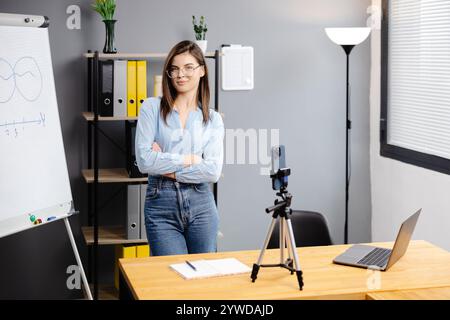 Junge Frau Mentorin nimmt Präsentationen auf, Webinar über Smartphone auf Stativ stehend, Lehrer Coach erklärt, hält Online-Unterricht, mit Telefon-Webc Stockfoto