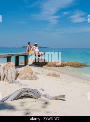 Die Sonne taucht am Sandstrand von Koh Munnork Island, während zwei Freunde sich auf dem Dock entspannen. Kristallklares Wasser und eine sanfte Brise sorgen für eine friedliche atmosphäre Stockfoto