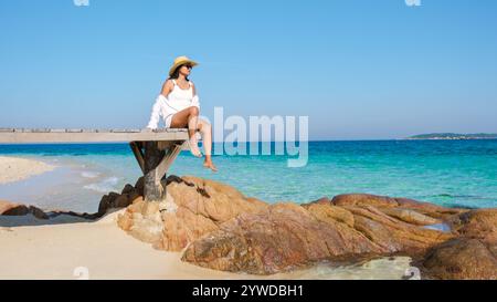 In einem ruhigen Moment auf Koh Munnork Island genießt eine Frau die Sonne auf einem hölzernen Pier. Das klare türkisfarbene Wasser und der glatte goldene Sand schaffen einen perfekten tropischen Zufluchtsort in Thailand. Stockfoto