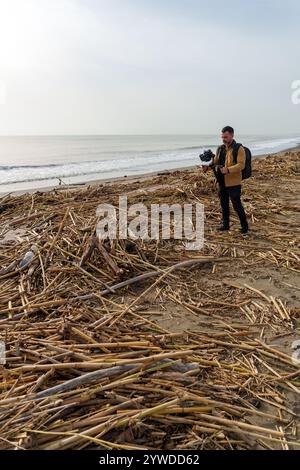 Der Videograf dokumentiert die Folgen einer Überschwemmung an einem Strand und nimmt Aufnahmen von Schutt und Vegetation auf, die an Land gespült wurden Stockfoto