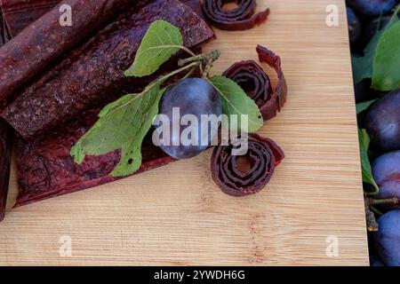 Pflaume mit Blättern. pflaumenpastilla rollt auf einem hölzernen Schneidebrett. Fruchtleder auf Holzoberfläche. Kopierbereich. Stockfoto