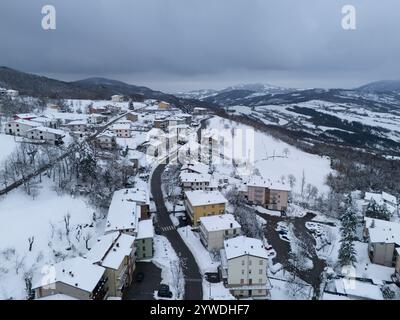 Aus der Vogelperspektive ist ein ruhiges Bergdorf eingebettet zwischen schneebedeckten Hängen und Bäumen, unter einem bewölkten Winterhimmel, das eine malerische Szene schafft Stockfoto