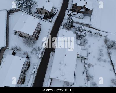 Aus der Vogelperspektive fängt ein ruhiges Bergdorf mit frischem Schnee ein, mit schneebedeckten Dächern, Bäumen und einer ruhigen Straße, die sich durch den Hou schlängelt Stockfoto