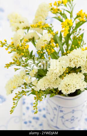 Ein wunderschönes Arrangement aus gelben und weißen Blüten, das anmutig in einer kunstvollen Keramikvase platziert wird, perfekt für die Aufhellung jeder Umgebung. Stockfoto