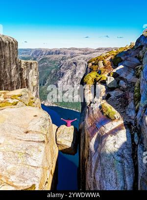 Eine Person steht am Rande des Kjeragbolten Rock in Norwegen und blickt auf die atemberaubende Landschaft darunter. Asiatische Frauen in Kjeragbolten Stockfoto