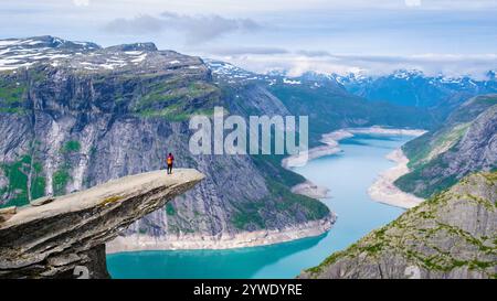 Eine einsame Wandererin steht am Rande der Trolltunga-Klippe in Norwegen mit Blick auf einen riesigen, blauen Fjord. Asiatische Frauen in Trolltunga, Norwegen. A Frau o Stockfoto