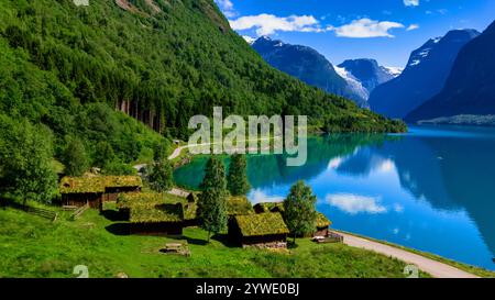 Grüne Hütten ruhen auf einem grasbewachsenen Hügel mit Blick auf einen ruhigen Fjord in Norwegen. Üppiges Grün bedeckt die umliegenden Berge, Lovatnet Lake Lodal Valley Stockfoto