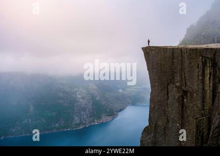 Ein einsamer Wanderer steht am Rande von Preikestolen, einer dramatischen Klippe mit Blick auf einen nebeligen Fjord in Norwegen. Preikestolen Norwegen. Konzept für psychische Erkrankungen Stockfoto