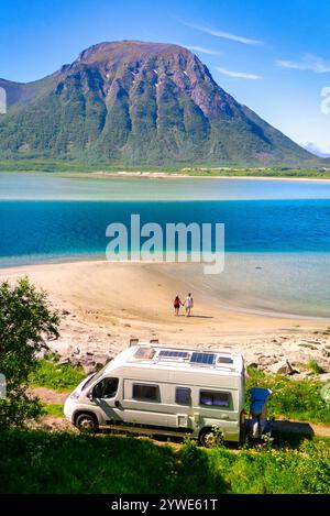 Ein paar Spaziergänge entlang eines unberührten Sandstrandes, ein Wohnmobil parkt in der Nähe, mit atemberaubendem Blick auf den norwegischen Fjord und einen majestätischen Berg im Hintergrund. Lofoten Norwegen Stockfoto