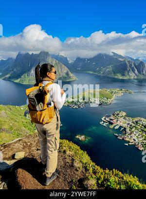 Eine Person bewundert die atemberaubende Aussicht auf den Fjord von einem Berggipfel, umgeben von zerklüfteten Gipfeln und ruhigem Wasser. Reinebringen Lofoten Norwegen. Asiatische Frauen tauschen einen Rucksack auf einem Berg Stockfoto