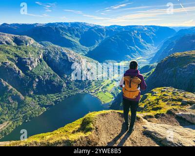 Ein einsamer Wanderer steht auf einem felsigen Felsvorsprung und bestaunt die atemberaubenden Fjorde und üppigen Täler Norwegens, umgeben von der Ruhe der Natur. Frau mit Stockfoto