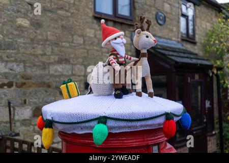 Red Royal Mail Briefkasten mit einer gestrickten Weihnachtsdekoration oder Garn Bombing gekrönt, in dem Dorf Hackleton, Northamptonshire, Großbritannien Stockfoto