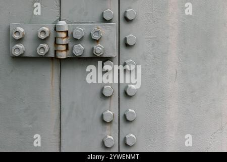 Graue Stahlwand mit Türscharnier und Bolzen, Verbindung von Metallteilen, abstraktes Foto im industriellen Hintergrund in Nahaufnahme Stockfoto