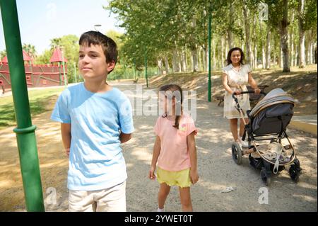 Eine Familie genießt einen sonnigen Tagesspaziergang im Park, bei dem Kinder spazieren gehen und ein Elternteil einen Kinderwagen schiebt. Die Szene fängt das Wesen der Familienbindung ein Stockfoto