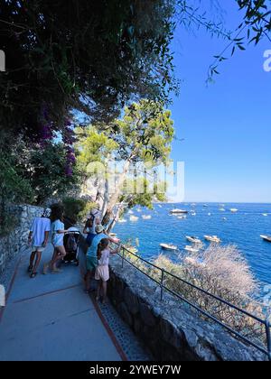 Die Familie macht einen gemütlichen Spaziergang entlang eines malerischen Küstenweges und genießt den atemberaubenden Blick auf Boote auf dem blauen Meer unter klarem Himmel. Eine ideale Einstellung für Stockfoto