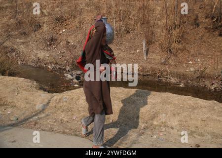 Srinagar, Indien. Dezember 2024. Die Frauen von Sonabanjran, einem abgelegenen Hügelland im Bezirk Pulwama in Südkaschmir, haben aufgrund der Temperaturen unter dem Gefrierpunkt große Schwierigkeiten. Da die Leitungswasserversorgung durch das Einfrieren der Versorgungsleitungen unterbrochen wurde, waren die Bewohner gezwungen, Trinkwasser aus einem gefrorenen Bach zu sammeln. (Foto: Nisar UL Haq Allaie/Pacific Press) Credit: Pacific Press Media Production Corp./Alamy Live News Stockfoto